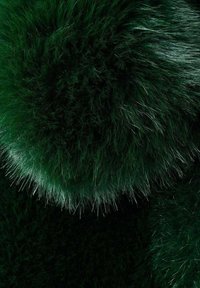 Tissu en fausse fourrure verte présentant une texture dense et duveteuse avec des nuances variées de vert et des fibres longues et douces très visibles, créant une profondeur visuelle.