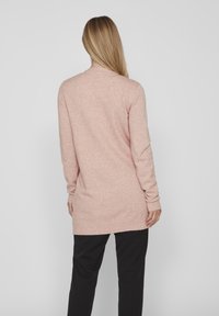 Rosa långärmad cardigan med ribbad nederkant och ärmslut, med en avslappnad passform och mjuk textur, bärs över mörka byxor.