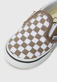 Hnedé a biele kockované slip-on topánky, vyrobené z plátna s bielou gumovou podrážkou a čiernym akcentom. Majú tesné sadnutie s elastickými bočnými panelmi.