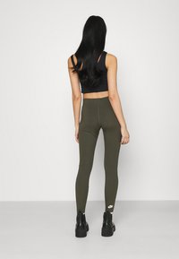 Olivgröna leggings i en åtsittande design med hög midja, kombinerade med en svart crop top. Har en diskret logotypdetalj nära vristen.