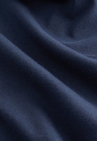 Tamsiai mėlynos spalvos medvilninis audinys su lygiu paviršiumi, kuriame matyti minkšti, švelniai krentantys klostės ir subtilios briaunos detalės. Puikiai tinka drabužiams ar tekstilės gaminiams.