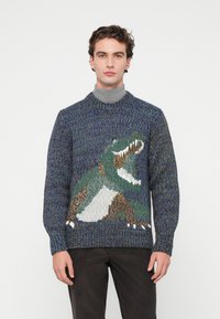 Pulover tricotat în nuanțe de albastru, cu un design de dinozaur în verde, brun și alb. Guler clasic rotund și mansete și tiv ribbate.