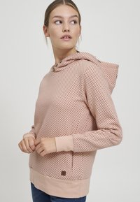 Sudadera con capucha en suave tela rosa con un patrón de puntos, puños acanalados y un parche de logo cosido cerca del dobladillo.