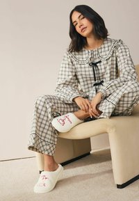 Čierne a biele kárované pyžamo s veľkým golierom a mašľou, doplnené o biele chlpaté papuče s červenou výšivkou.