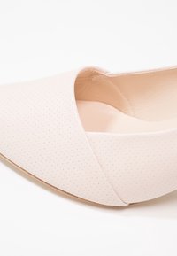 Chaussure plate en cuir rose perforé avec un bout pointu et une coupe asymétrique le long du cou-de-pied, dotée d'une doublure intérieure lisse.