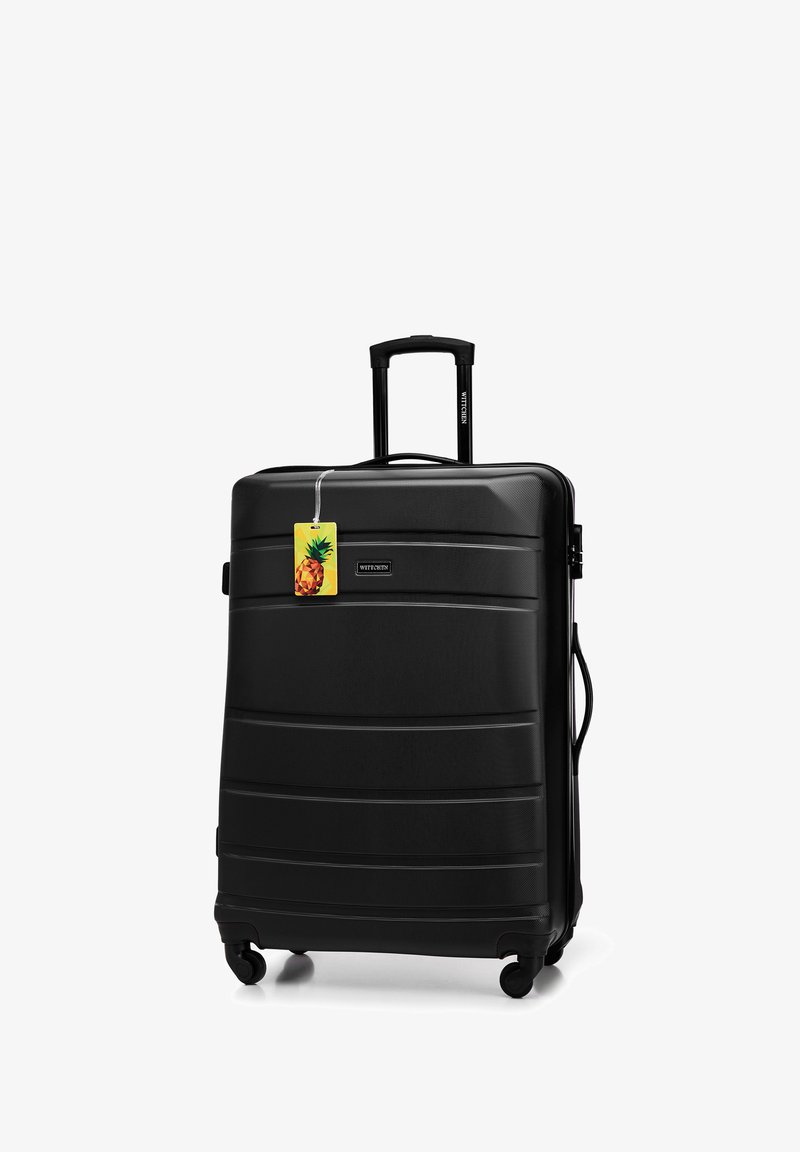 Black hard-shell suitcase with horizontal ridges, a retractable handle, four wheels, and a bright pineapple luggage tag attached.