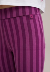 Lilla triibuline leggins, mis on valmistatud venivast kangast. Omab laia vööd ja külgpinnal väikest sildi, millel on tähtede aktsent.