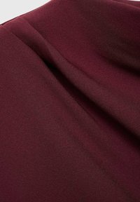 Burgundy tyg med en slät textur, med draperade veck som skapar en subtil glans och visuell djup.