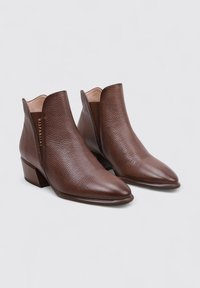 Botas de tobillo de cuero marrón con puntera puntiaguda, superficie texturizada y un pequeño tacón cuadrado. Diseño clásico con recortes en los laterales.