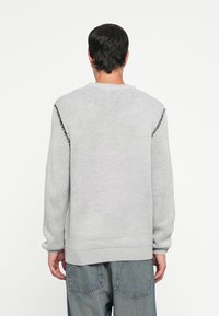 Grijze gebreide trui met lange mouwen, ronde hals en tekstuurafwerking. Heeft zwarte accenten langs de schoudernaad. Losse pasvorm en casual ontwerp.