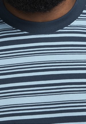 Gros plan sur le cou et le haut de la poitrine d’une personne portant une chemise rayée horizontalement bleu marine et bleu clair.