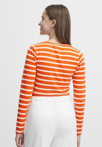 Långärmad T-shirt med orange och vita horisontella ränder, tillverkad av mjukt tyg. Bärs med högmidjade vita byxor, rundad halsringning.