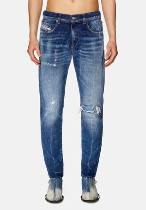 Herreblå slidte denimjeans med falmede og revnede detaljer, båret med tofarvede blå og grå støvler.