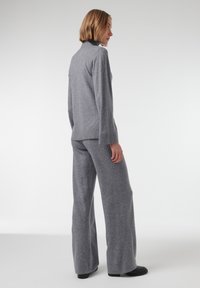 Grijze gebreide trui en bijpassende wijde broek, met een hoge kraag, geribbelde manchetten en een zachte textuur tegen een effen achtergrond.