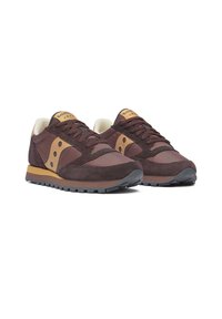 Un paio di sneaker Saucony Jazz marroni e beige con tomaia in camoscio e nylon, design con lacci e suola in gomma, vista laterale inclinata su sfondo bianco.