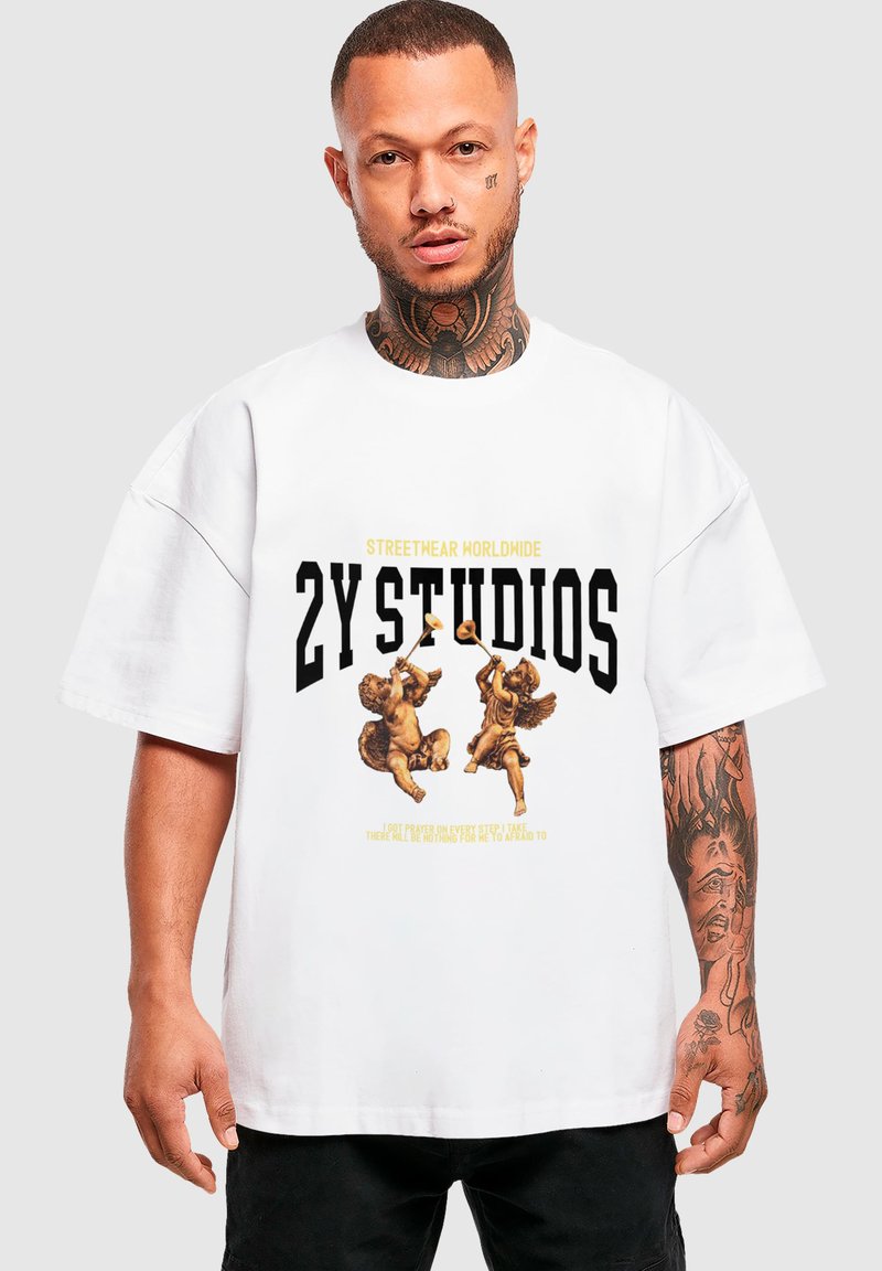Fehér, oversize T-shirt, amelyen két cherub grafikája, vastag fekete felirat "2Y STUIDOS" és alatta sárga kiemelő szöveg található.
