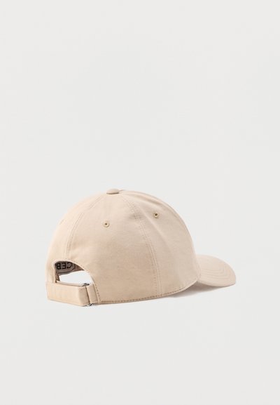 Casquette de baseball beige en coton avec sangle réglable et boucle métallique vue de dos sur fond blanc.