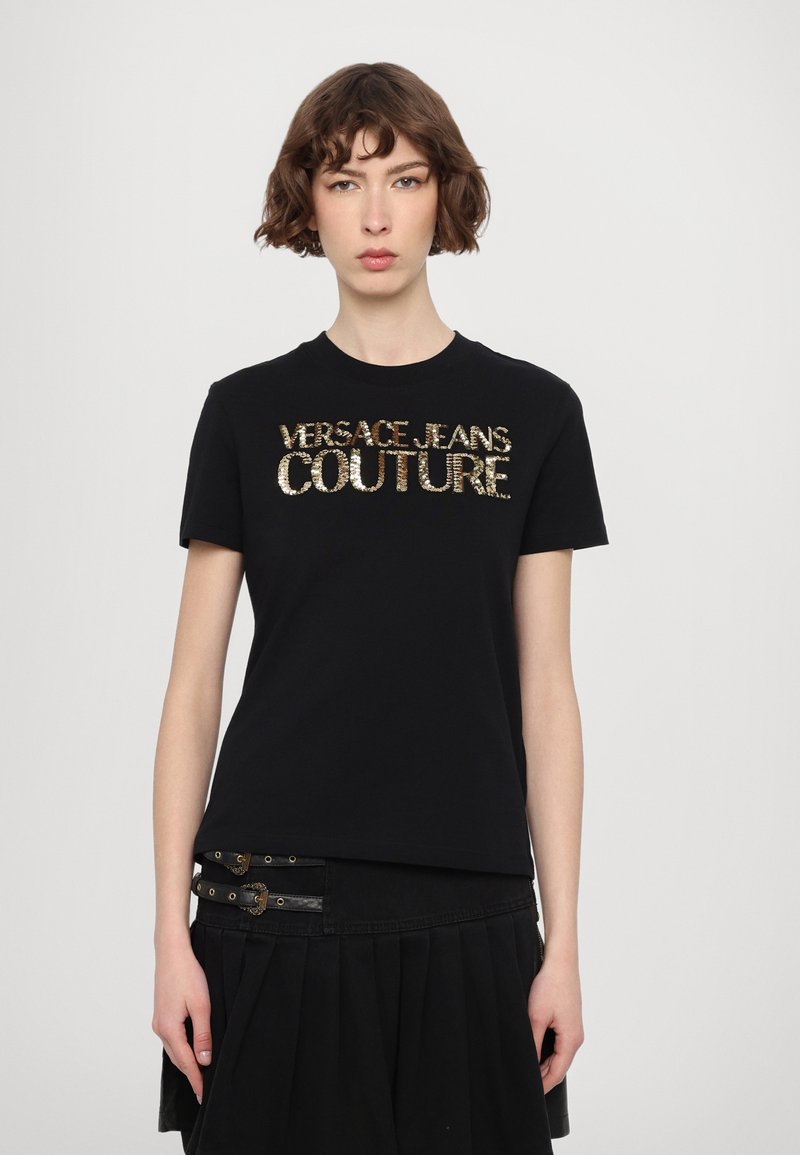 Črna bombažna majica s kratkimi rokavi, ki vsebuje zlato bleščičasto logo "VERSACE JEANS COUTURE". Prilegajoča zasnova s klasifikacijo določenega okroglega izreza.