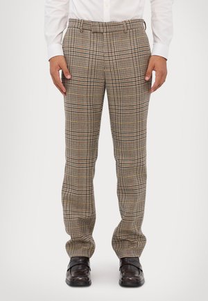 Karierte Hosen in Brauntönen und Beige, mit lässiger Passform, Gürtelschlaufen und weichem Material, kombiniert mit schwarzen Schuhen.