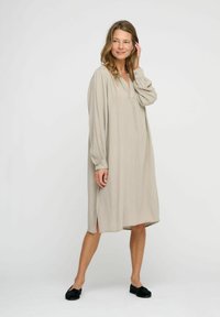 Beige midi dress with a loose fit, long sleeves, a V-neckline, side slits, and soft texture, paired with black shoes.