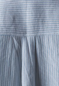 Ljusblå randig tyg med horisontella och vertikala linjer, med veck längs den nedre delen och en slät, mjuk textur.