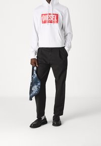 Vit hoodie med röd "DIESEL"-logotyp, svarta byxor och en tie-dye axelväska. Svarta skor med texturerad yta. Avslappnad outfit.