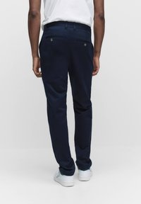 Marineblaue Hose mit geradem Schnitt, aus Baumwolle, zwei Gesäßtaschen und metallischen Knopf-Details, kombiniert mit weißen Sneakers.