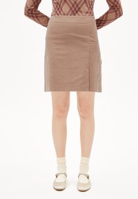 Brauner Cordrock mit gerader Silhouette, versehen mit einer Seitentasche, getragen mit hellfarbenen Socken und metallischen Mary Jane Schuhen.