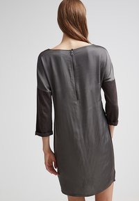 Robe grise à manches trois-quarts, avec une texture satinée, un éclat subtil et une fermeture éclair verticale au dos. Les manches plus foncées contrastent avec le corps.