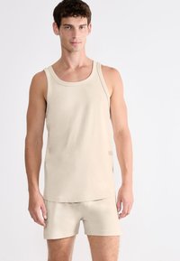 Débardeur en coton beige avec un col rond, présentant une texture lisse et un logo minimaliste, accompagné de shorts assortis.