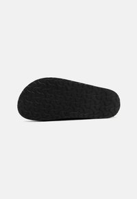 Semelle de chaussure en caoutchouc noir avec un motif de texture ondulée, présentant une forme arrondie et une légère courbure au niveau des orteils. Marquages de taille visibles.