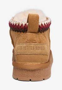 Botte en suède beige avec une semelle en caoutchouc texturé, doublure en fourrure et accents tressés en bourgogne et crème, dotée d'une languette arrière pour un enfilage facile.