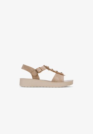 Beige suede sandal with a flat sole, featuring a narrow ankle strap, buckle detail, and embellishments across the front.