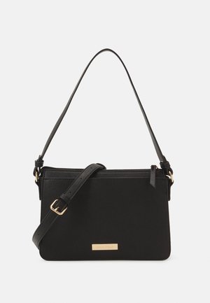 Sac à bandoulière noir en matière synthétique texturée, doté d'une sangle réglable, de ferrures couleur or et d'une plaque avec le logo de la marque sur le devant.