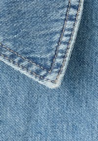 Gros plan d'un tissu denim bleu avec des coutures orange détaillées le long d'un bord plié.