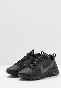 Svarta träningssko med en texturerad yta, med en grå Nike-swoosh, lätt design och rund sula med synliga dämpningspunkter.