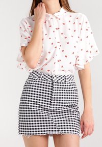 Vit blus med röd läppmönster och korta volangärmar, tillsammans med en svartvit rutig denimkjol med framknäppning.