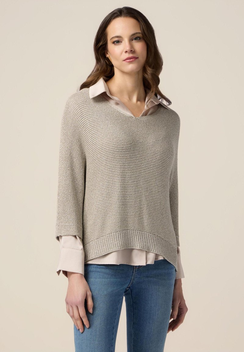 Lysegrå strikket sweater med løs pasform, lange ærmer og bred halsudskæring, lagd over en kremfarvet skjorte med krave og denim jeans.