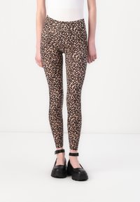 Leopárdmintas leggings puha, rugalmas anyagból, magas derekú és testhez simuló fazonban, fekete, vastag talpú cipőkkel párosítva.