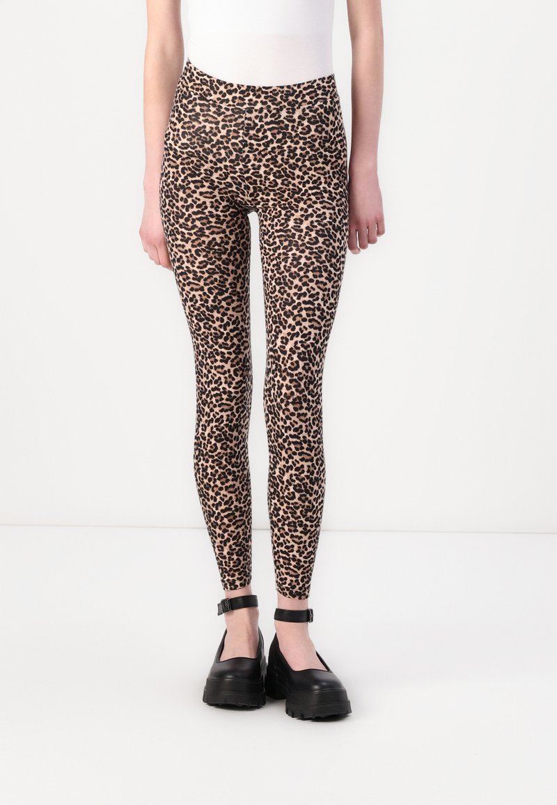 Leopárdmintas leggings puha, rugalmas anyagból, magas derekú és testhez simuló fazonban, fekete, vastag talpú cipőkkel párosítva.