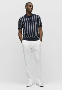 Marinblårandig polotröja med korta ärmar, kombinerad med vita byxor och sneakers. Polotröjan har ribbad krage och ärmslut.