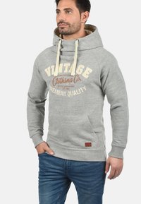 Gray hoodie with a large front pocket, drawstrings, and vintage printed text in beige and brown. Features a textured fabric and ribbed cuffs.