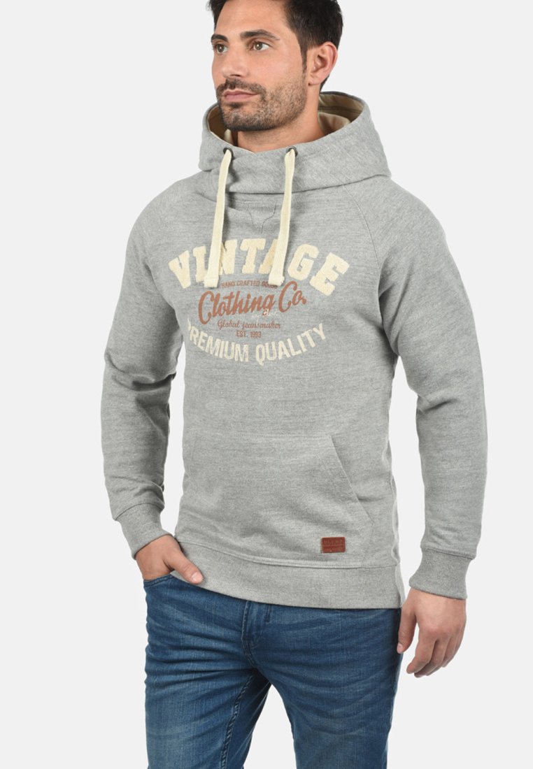 Grå hoodie med en stor frontlomme, snore og vintagedrukket tekst i beige og brun. Har et struktureret stof og ribbede manchetter.