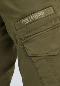 Olivnozeleni vojaški hlače iz teksturiranega blaga, z mošnjo na žepu in logotipom "PME LEGEND" na pasu. Očitne šivane podrobnosti.