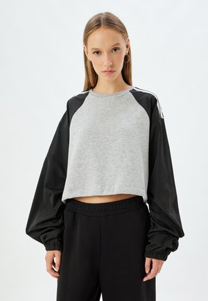 Korte sweatshirt met een grijze katoenen romp en zwarte nylon mouwen, voorzien van elastische manchetten en witte accentstrepen op de schouders.