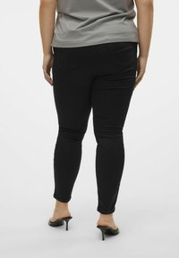 Crne skinny traperice izrađene od elastine tkanine. Imaju dva stražnja džepa, glatku teksturu i kombiniraju se sa sivoj majici i crnim potpeticama.