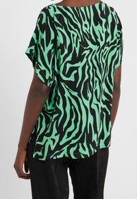 Svart tröja med grönt zebramönster, batwingärmar, lös passform och rundad halslinning. Mjuk tygkänsla.