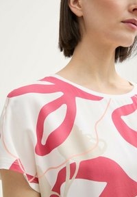 Kurze Bluse aus weißem Stoff mit abstrakten rosa und beigen Mustern. Glatte Textur mit rundem Ausschnitt und lässiger Passform.