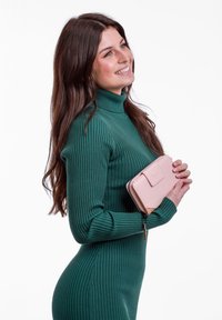 Ribbed green sweater dress, fitted shape, paired with a light pink leather wallet featuring a zip closure and snap fastener.