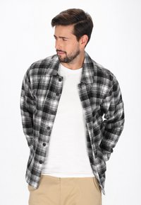 Musta-valkoinen ruudullinen flanellipaita, jossa on pitkät hihat, napit edessä ja hieman oversize-istuvuus, sen päällä valkoinen t-paita.